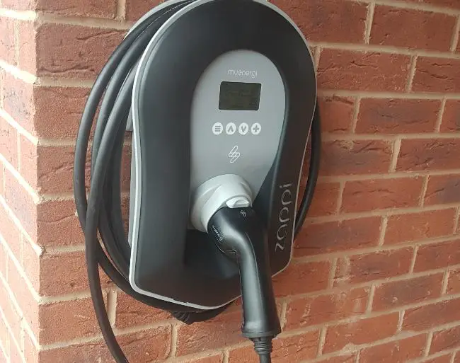 Black electrical vehicle charger with tethered lead installed on brick wall by Shrewsbury electrician.